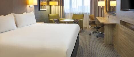 A hotel room with a large bed, a desk with a chair, a small round table, and a TV.