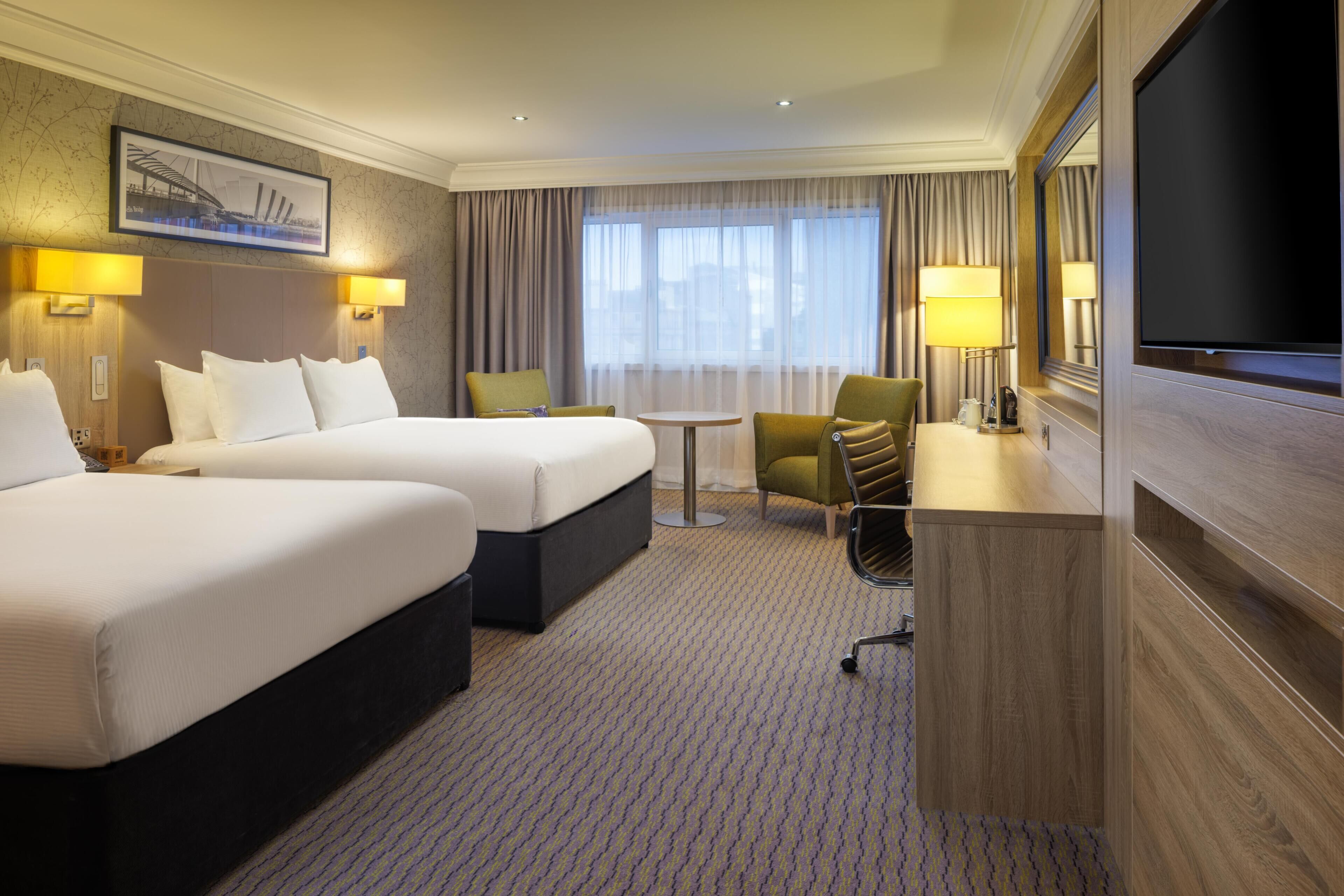A hotel room with two beds, a desk, a chair, a TV, and a window with curtains.