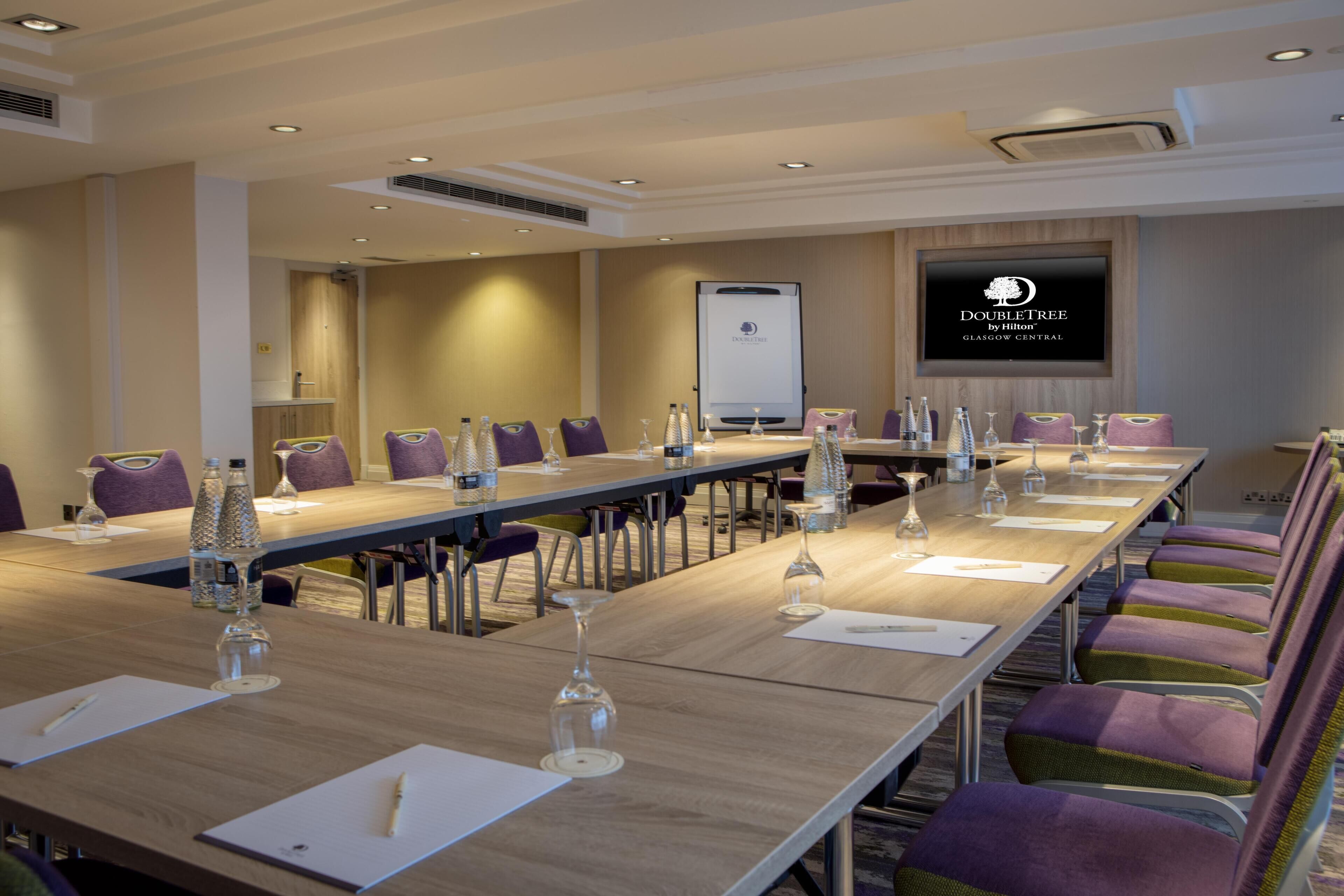 A conference room with a long table, chairs, and a screen displaying the DoubleTree by Hilton logo.
