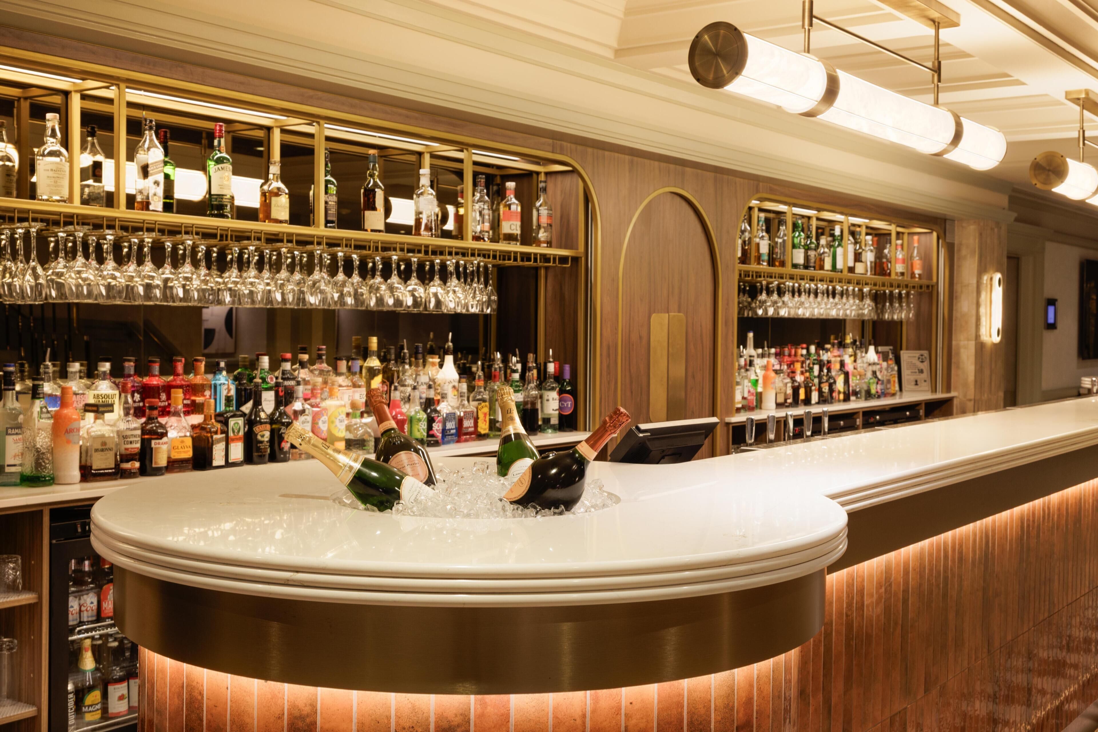 Una zona de bar con una barra curva, estantes llenos de botellas de licores y vasos.