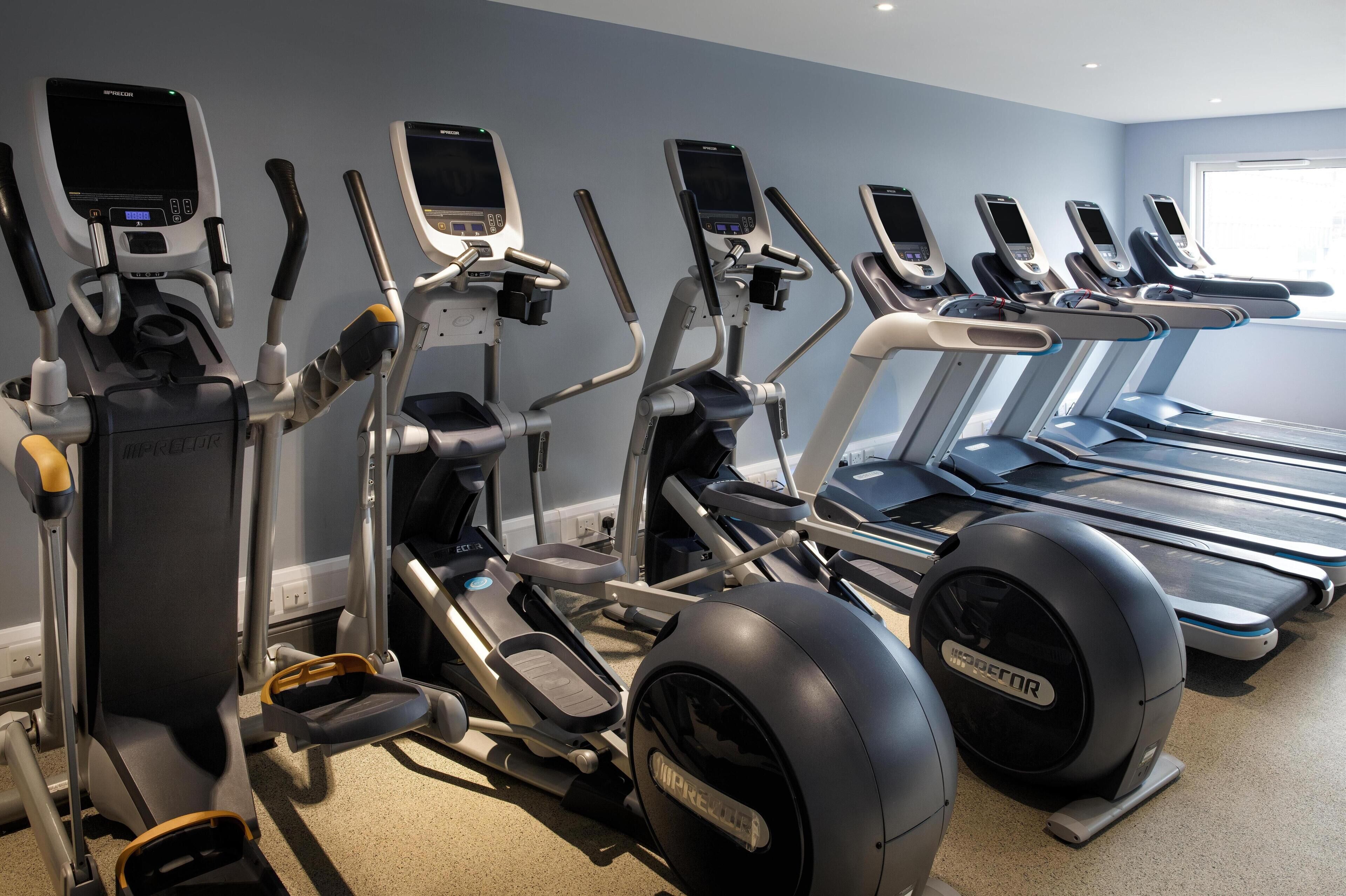 A gym with various exercise machines, including ellipticals and treadmills, arranged in a row.