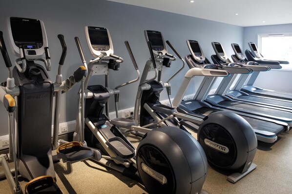 Un gimnasio con diversas máquinas de ejercicio, incluyendo elípticas y cintas de correr, dispuestas en fila.
