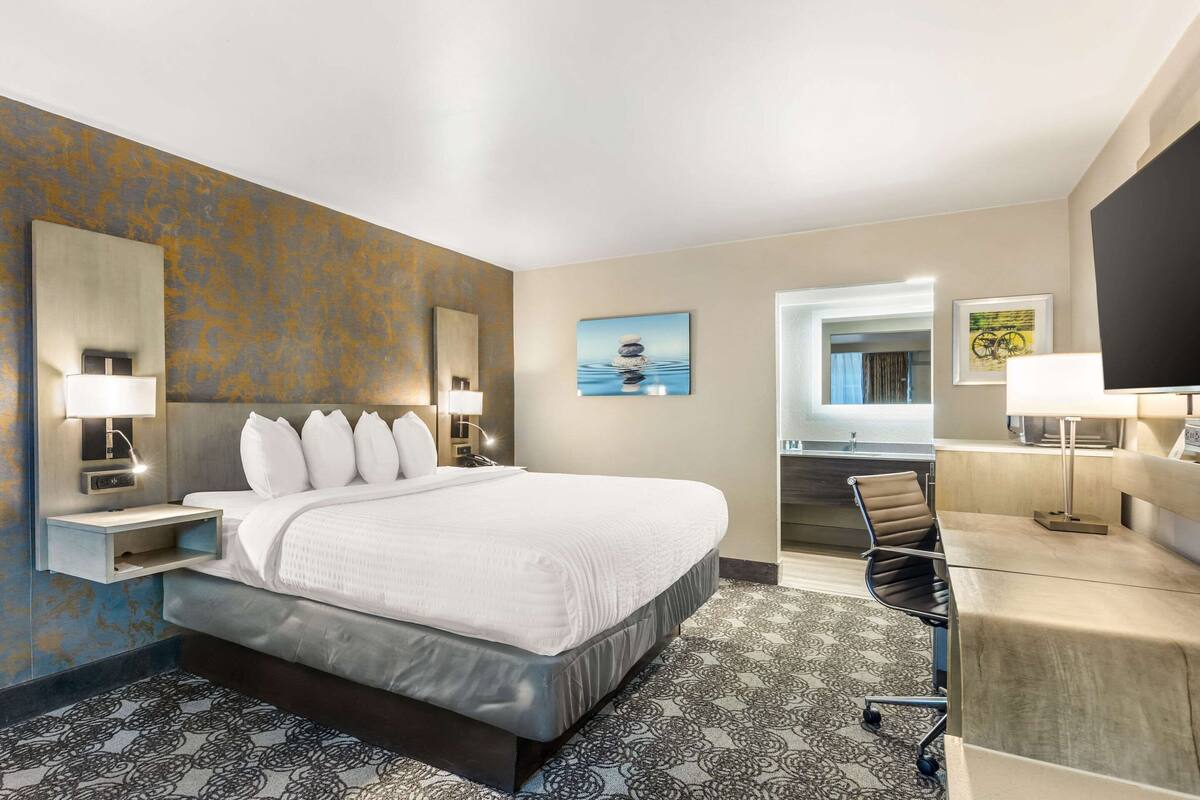 Une chambre d’hôtel avec un grand lit, des lampes de chevet, un bureau avec une chaise, une télévision et des œuvres d’art accrochées aux murs.
