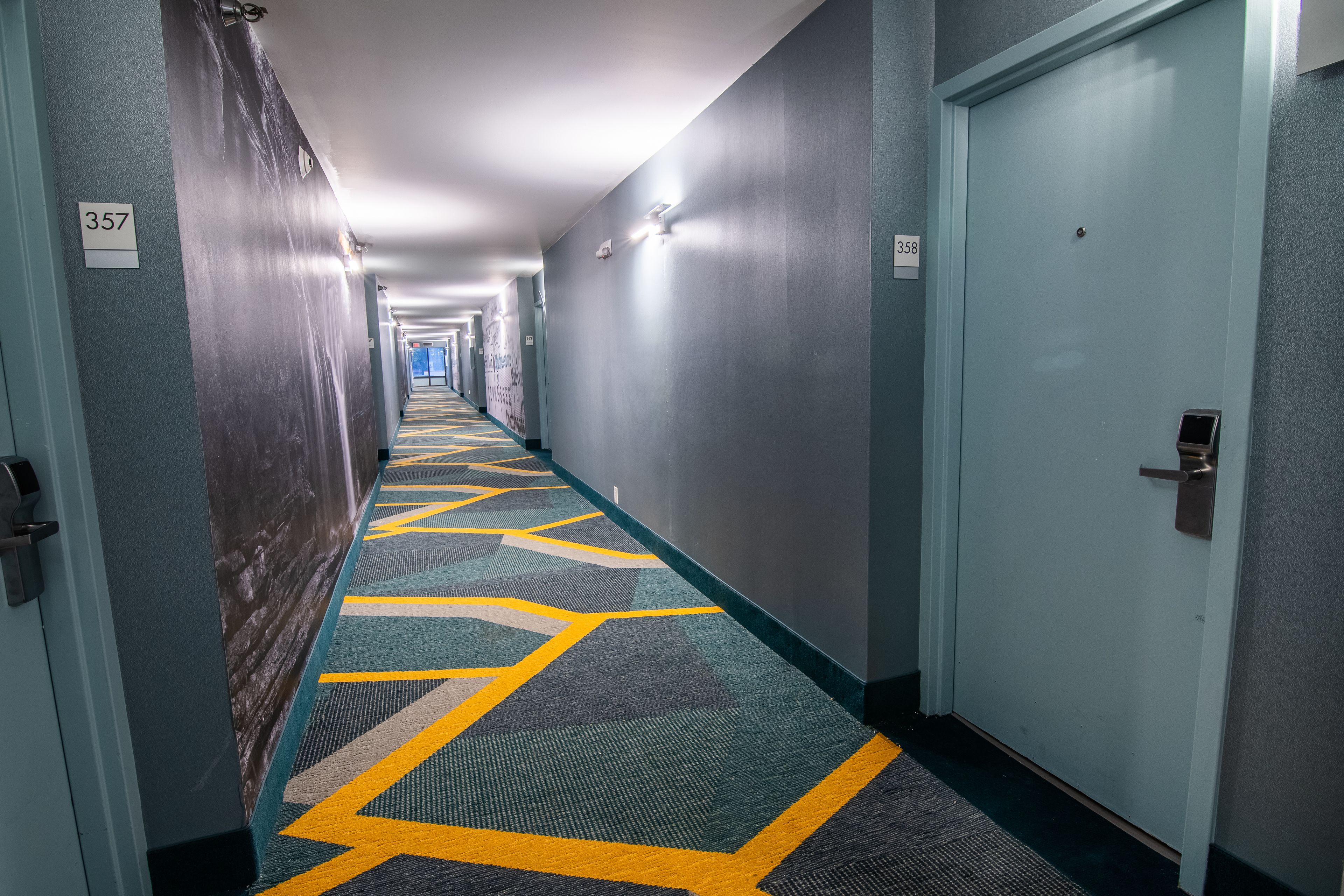 A hotel hallway with carpeted floors, doors numbered 357 and 358, and a light-colored wall.