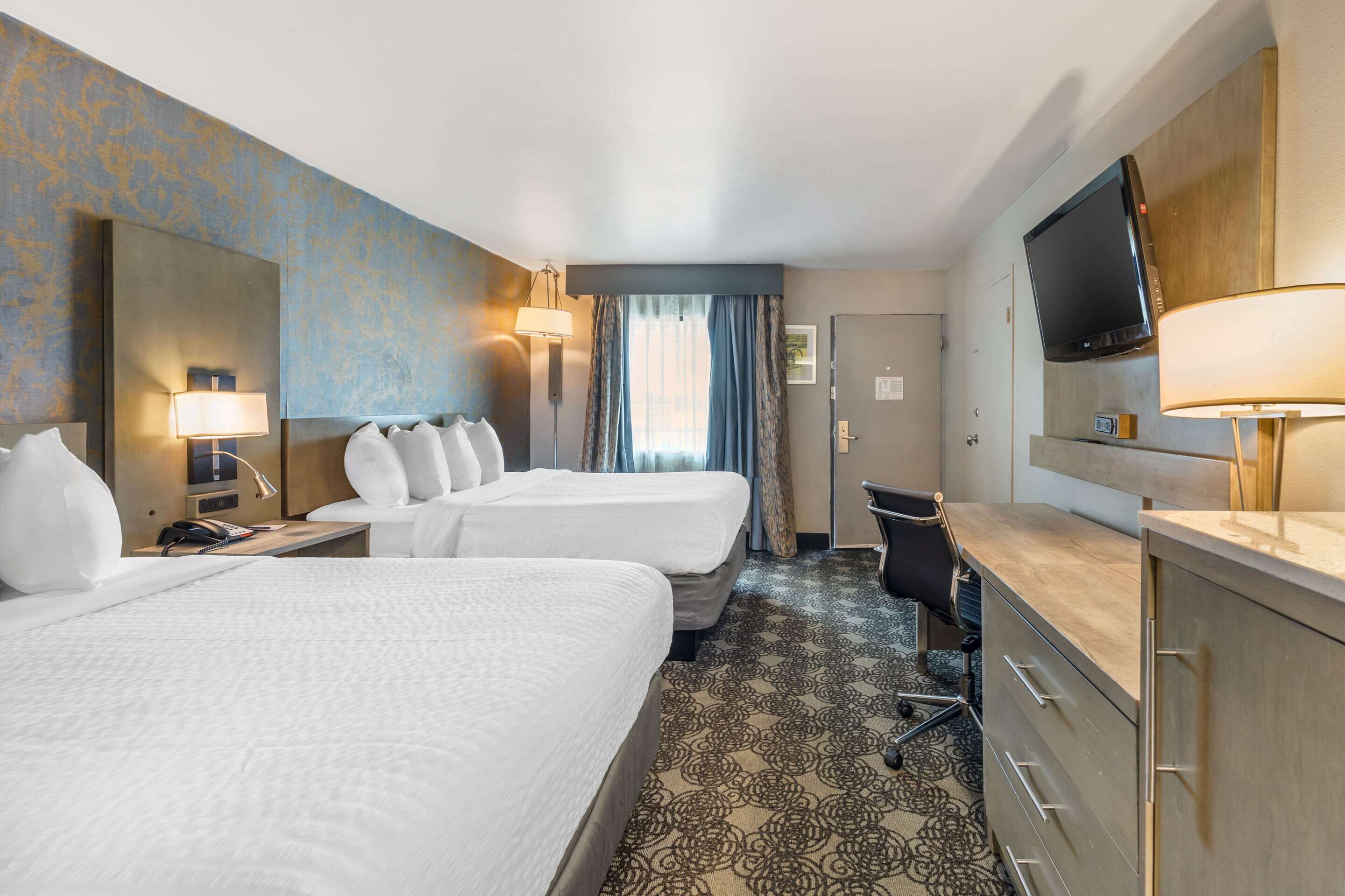 Habitación de hotel con dos camas, un escritorio, televisor y baño.