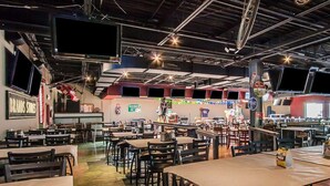 A spacious indoor dining area with multiple tables and chairs, high ceilings with exposed beams, and various signs and decorations on the walls.