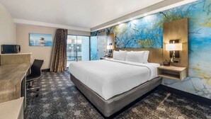 Une chambre d’hôtel avec un grand lit, un bureau et une chaise. Il y a une fenêtre avec des rideaux, un mur orné d’un motif abstrait bleu et une table de chevet avec une lampe.