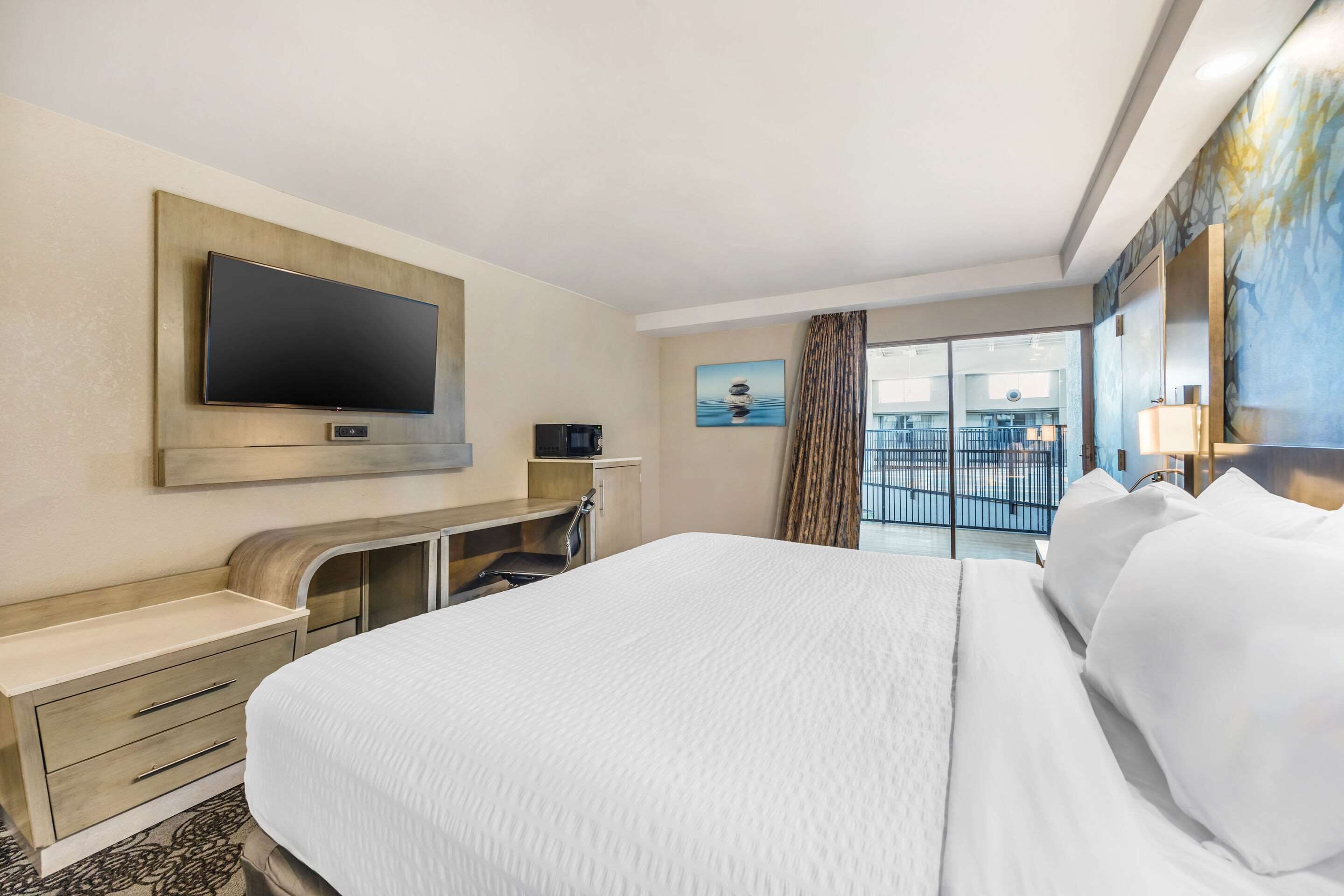 A hotel room with a large bed, a flat-screen TV mounted on the wall, a desk with a chair, and a window with a view of the city.