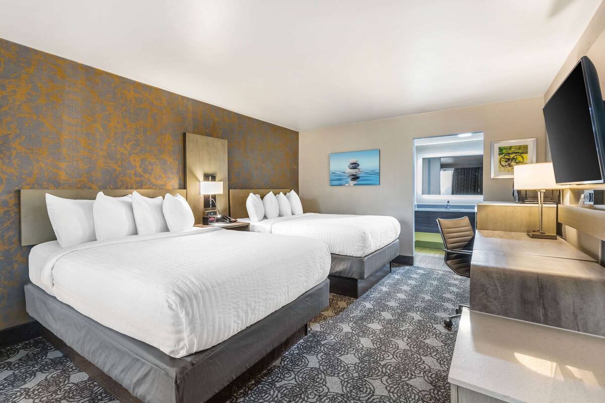 Une chambre d’hôtel avec deux lits, un bureau, une chaise, une télévision et une fenêtre.