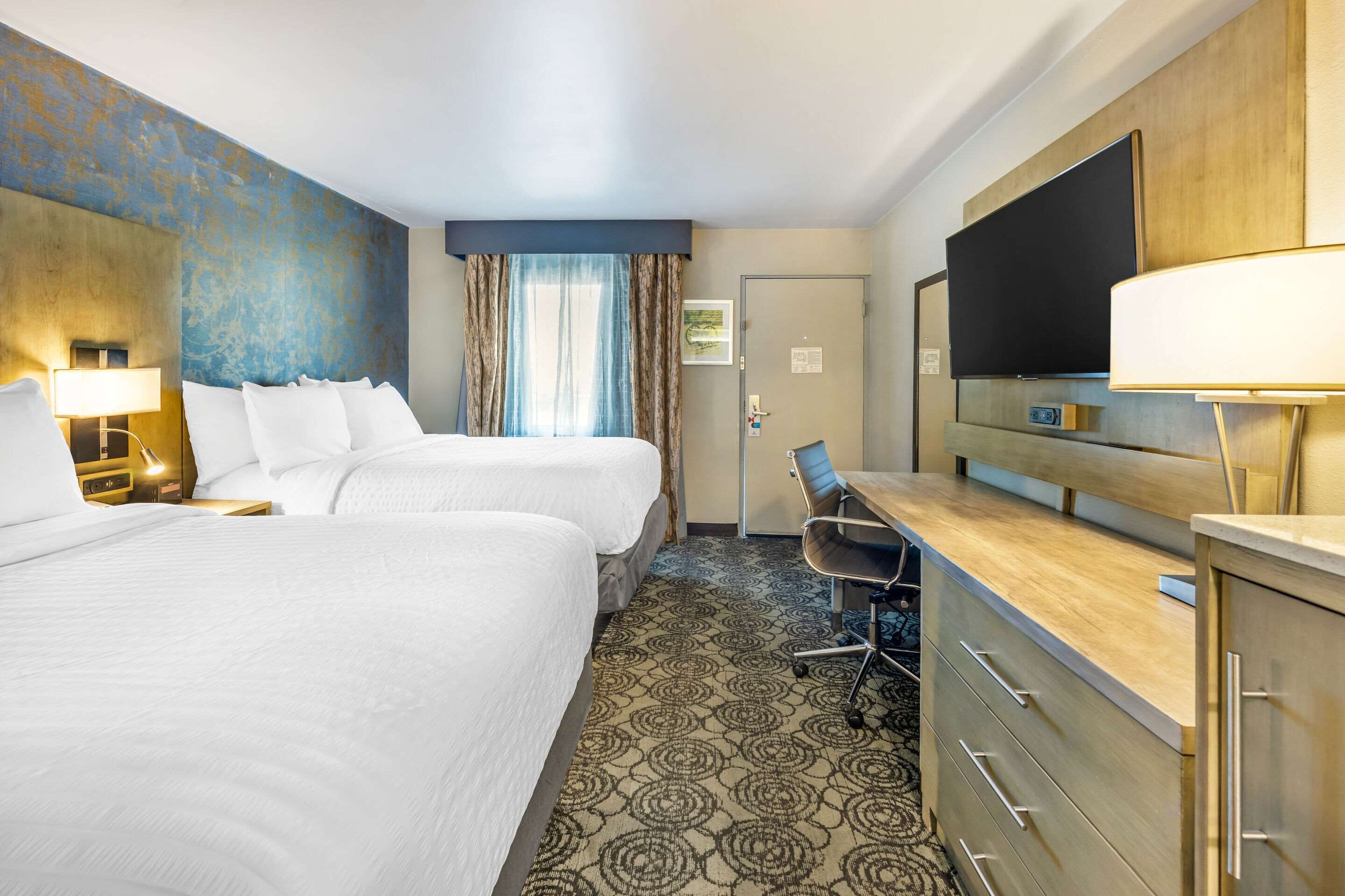 Habitación de hotel con dos camas, un escritorio con silla, televisor y minibar.