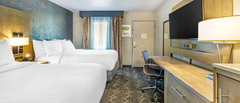 Habitación de hotel con dos camas, un escritorio con silla, televisor y minibar.