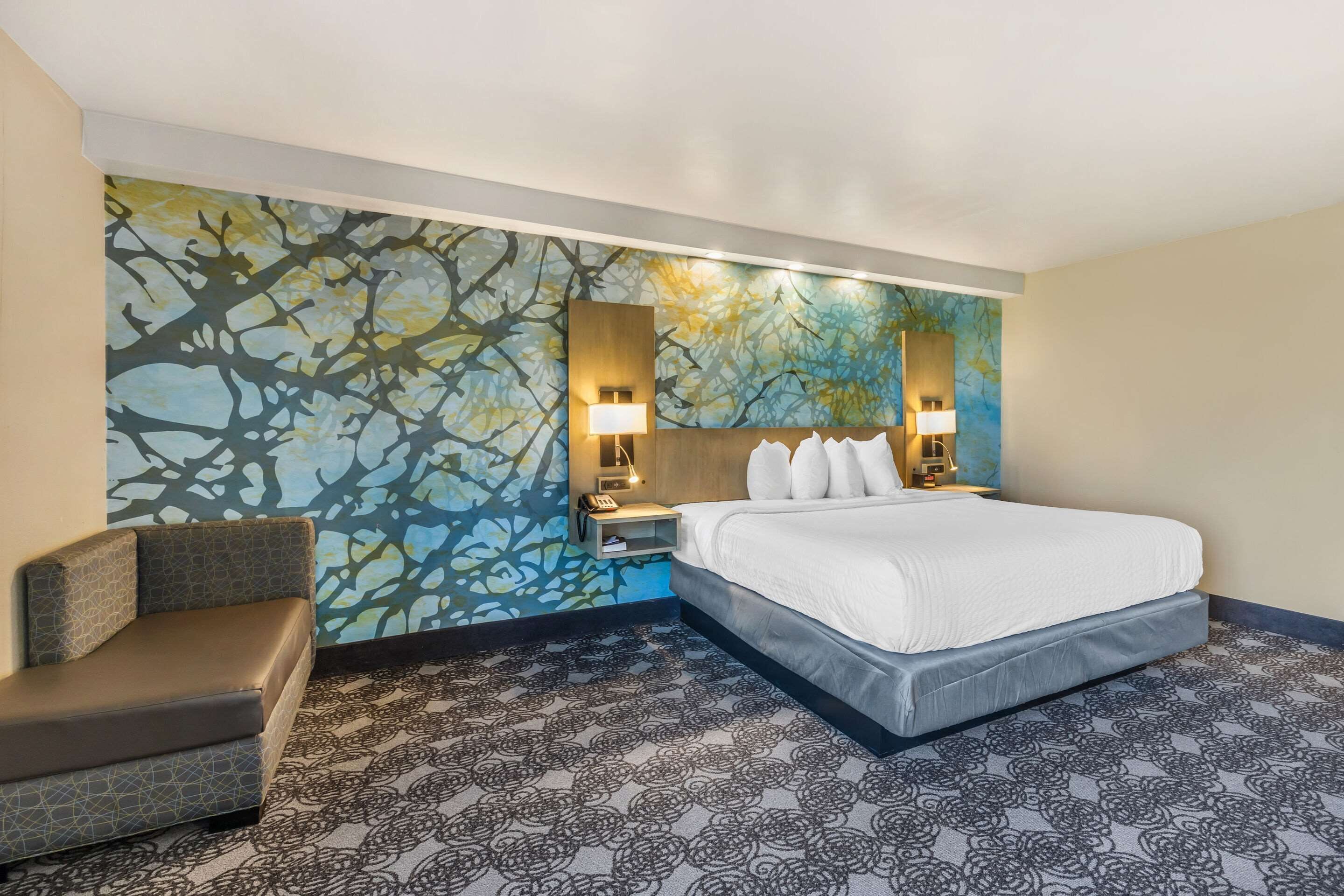 A hotel room with a large bed, a seating area, and a wall with a tree branch pattern.