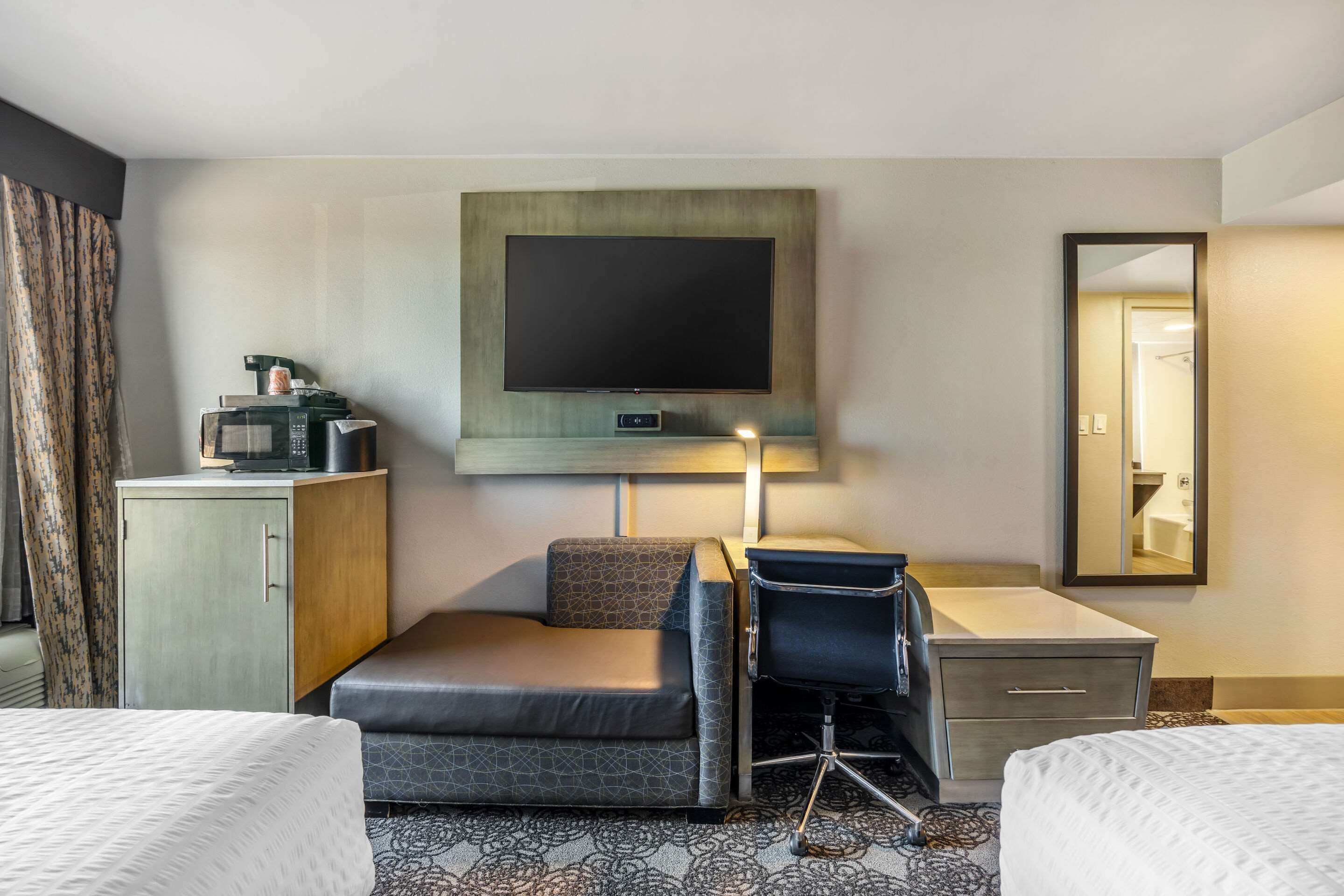 A hotel room with a bed, a desk with a chair, a television, a microwave, a cabinet, and a mirror.