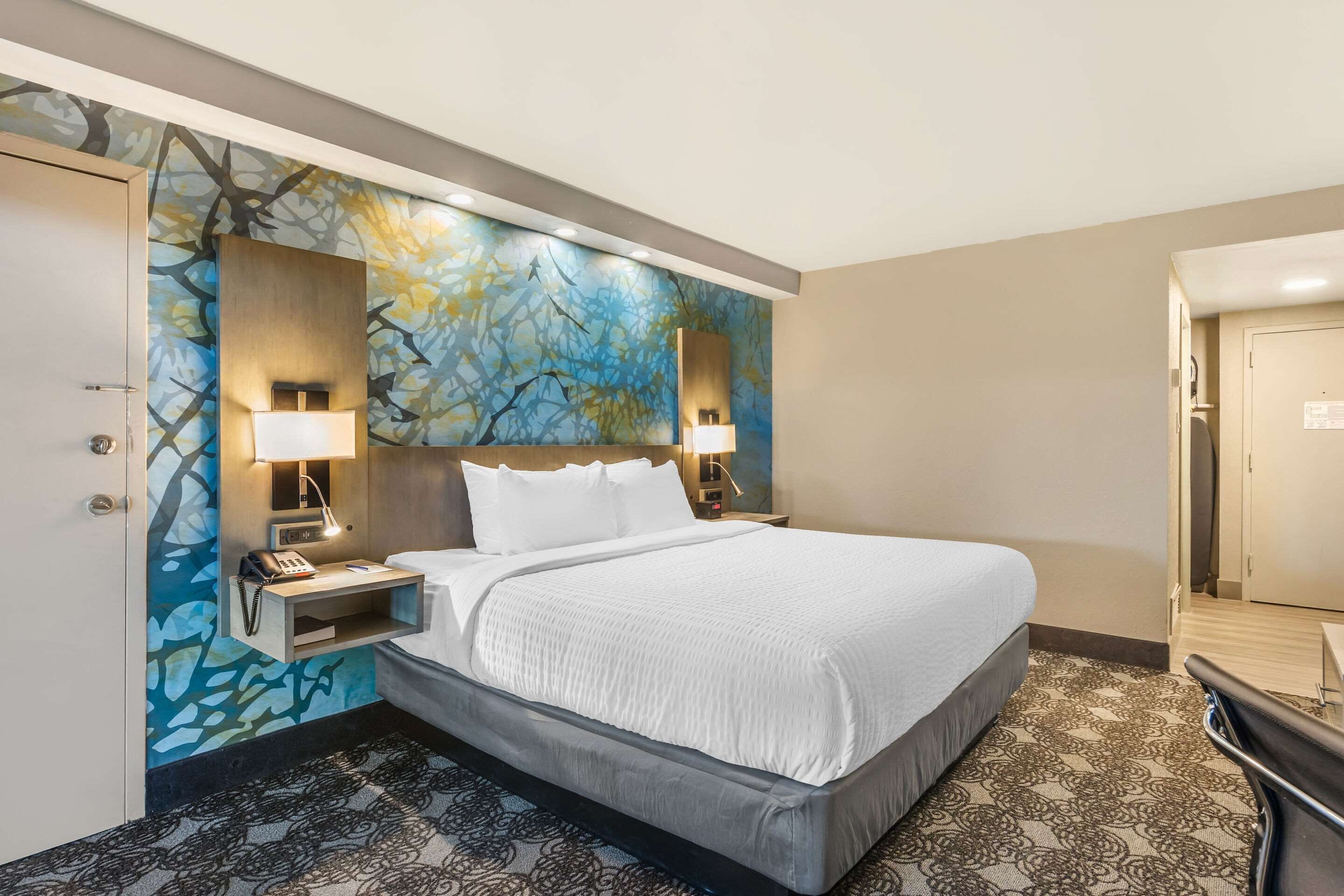 A hotel room with a large bed, two bedside lamps, a nightstand, and a wall mural.