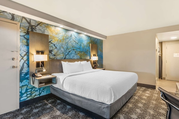 Una habitación de hotel con una cama grande, dos lámparas de noche, una mesita de noche y un mural en la pared.