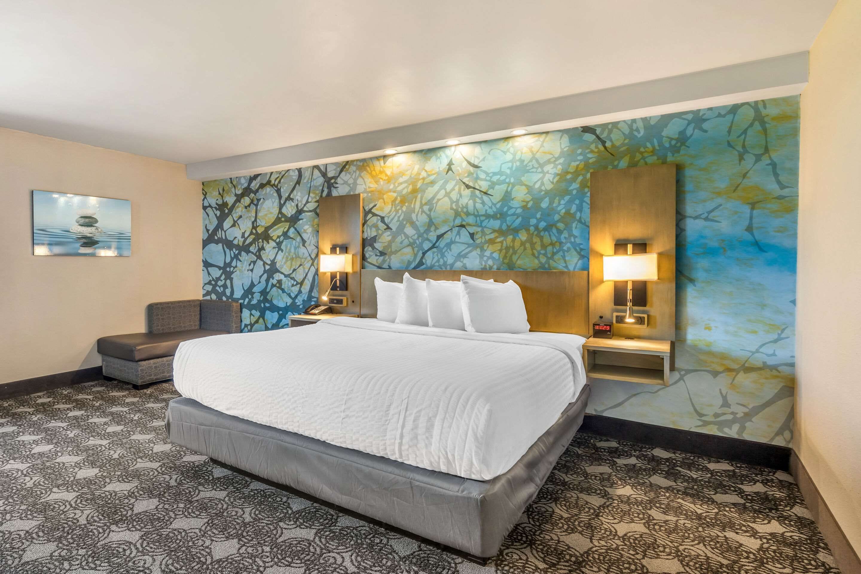 Ein Hotelzimmer mit einem großen Bett, einem Sessel, einem Schreibtisch und einer Wand mit einer Wandmalerei von Baum und Wasser.
