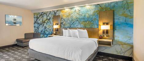 Ein Hotelzimmer mit einem großen Bett, einem Sessel, einem Schreibtisch und einer Wand mit einer Wandmalerei von Baum und Wasser.