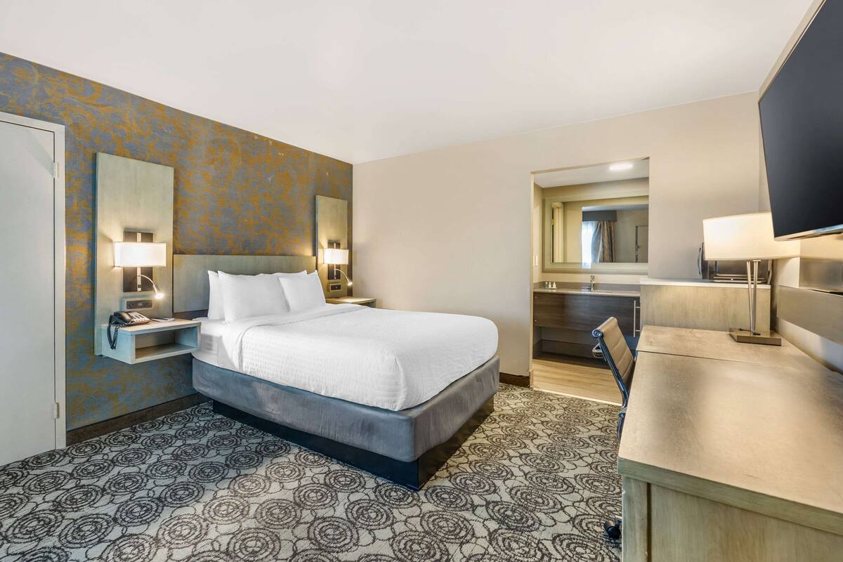 Une chambre d’hôtel comprenant un lit, des tables de chevet, un bureau, une chaise, une télévision et une salle de bain.