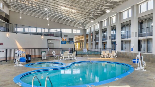 Une piscine intérieure divisée en deux zones distinctes, entourée d’un sol carrelé et équipée de rampes de sécurité.