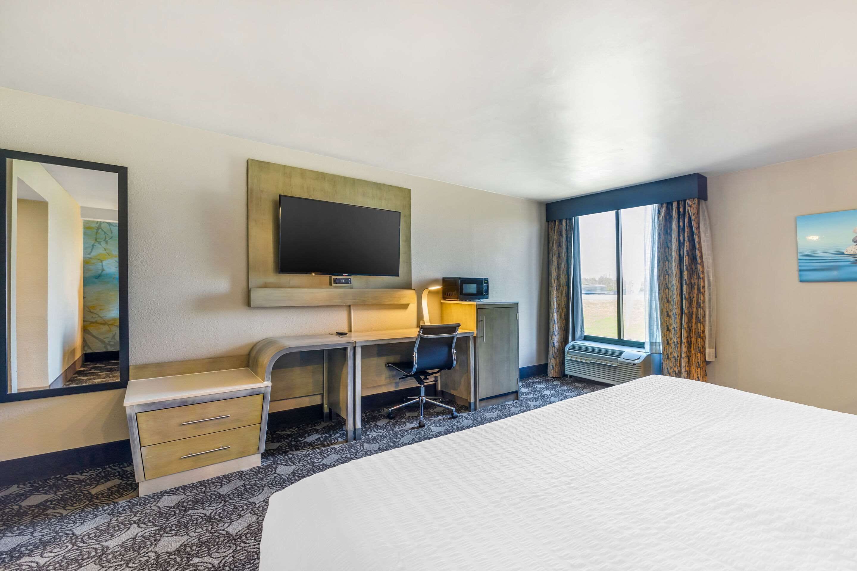 Hotelkamer met een groot bed, bureau met stoel, flatscreen televisie, spiegel en raam met gordijnen.