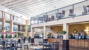 Un grand espace intérieur comprenant plusieurs tables et chaises, un coin cuisine avec des machines à café, et un balcon aménagé avec des sièges.