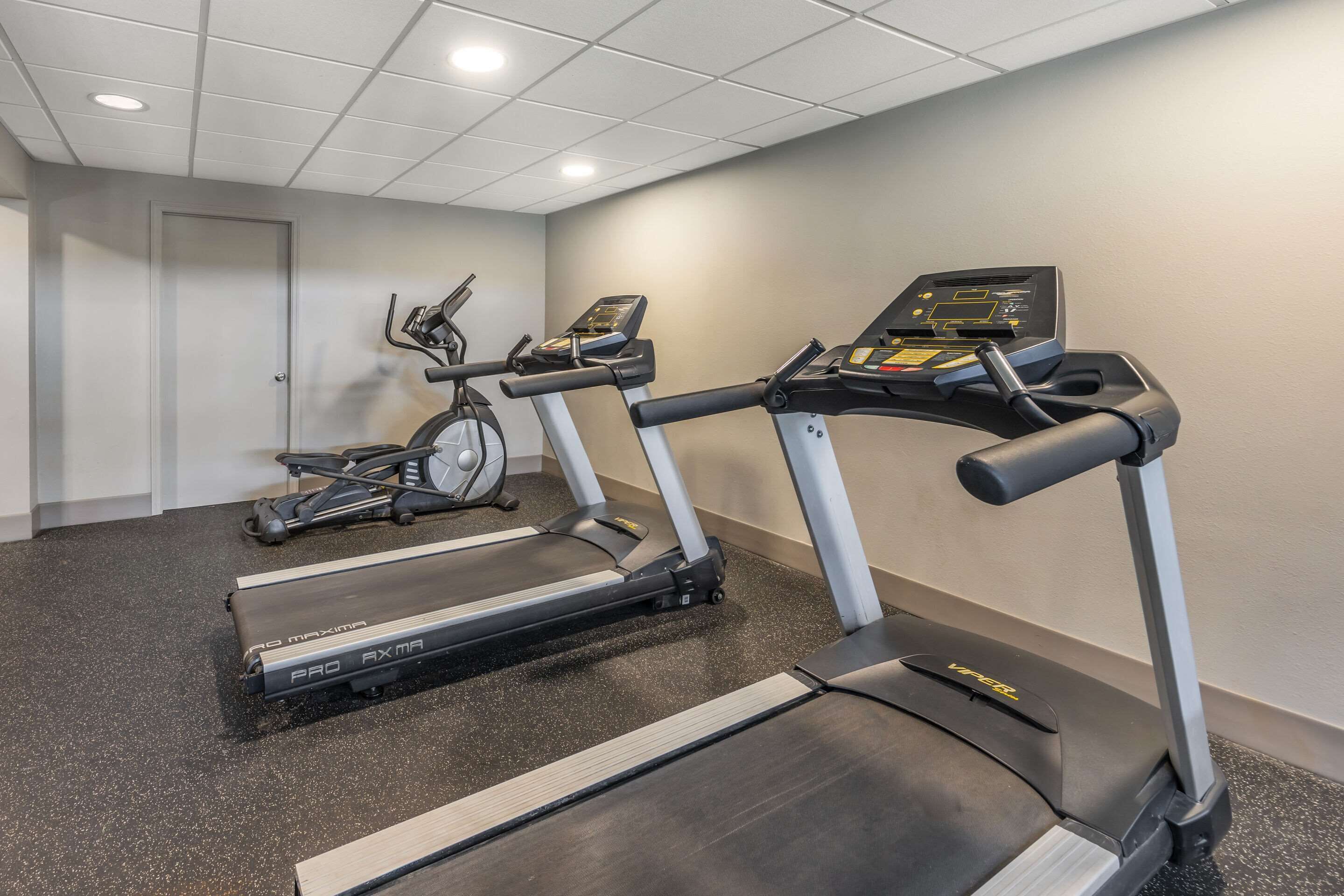 Un gimnasio con cintas de correr, bicicletas estáticas y una máquina de remo.