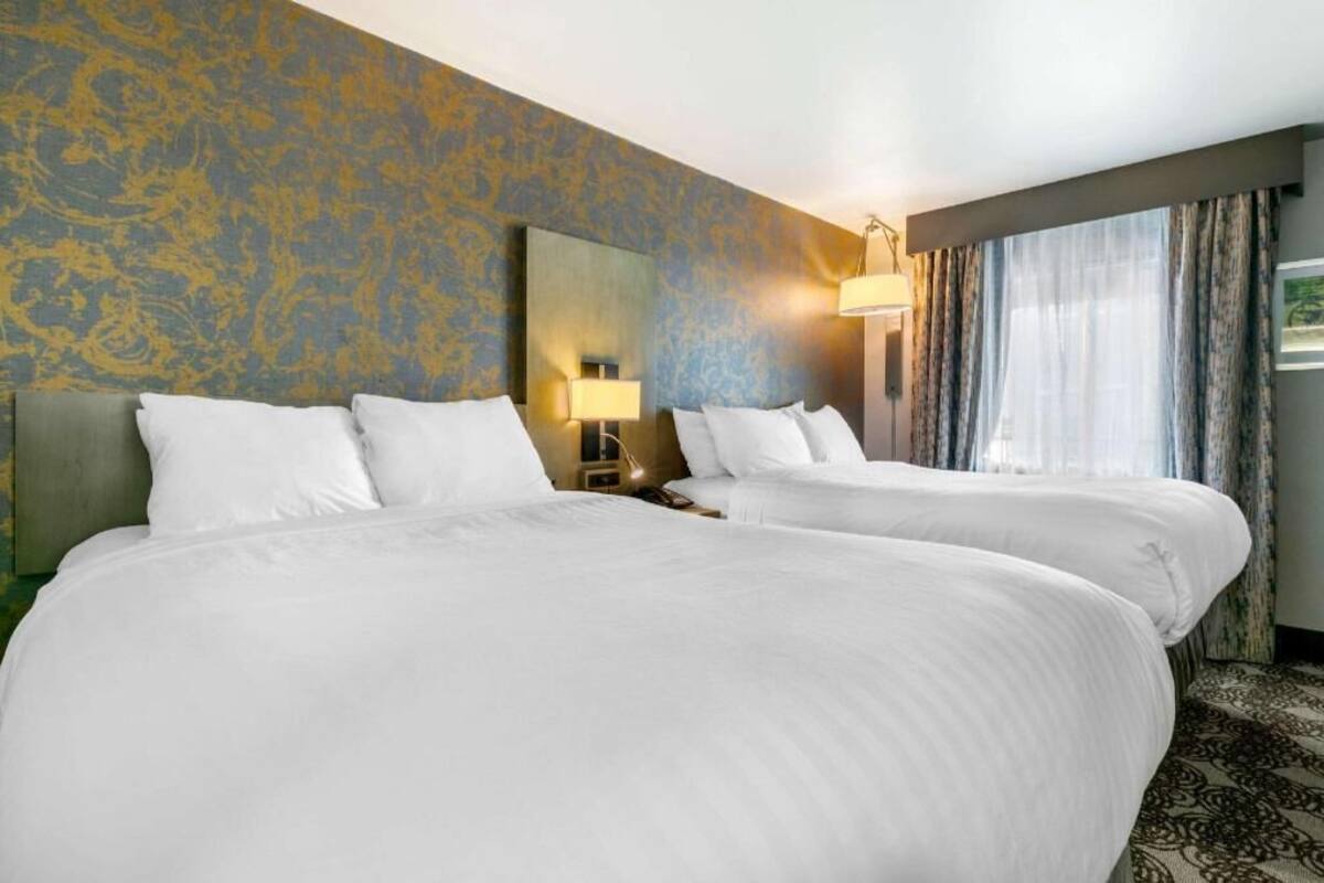 Une chambre d’hôtel avec deux lits, une table de chevet, une lampe et une fenêtre avec des rideaux.