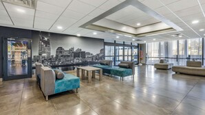 Un hall d’entrée spacieux, doté de sièges modernes, d’une fresque représentant un paysage urbain et de grandes fenêtres offrant une vue panoramique.