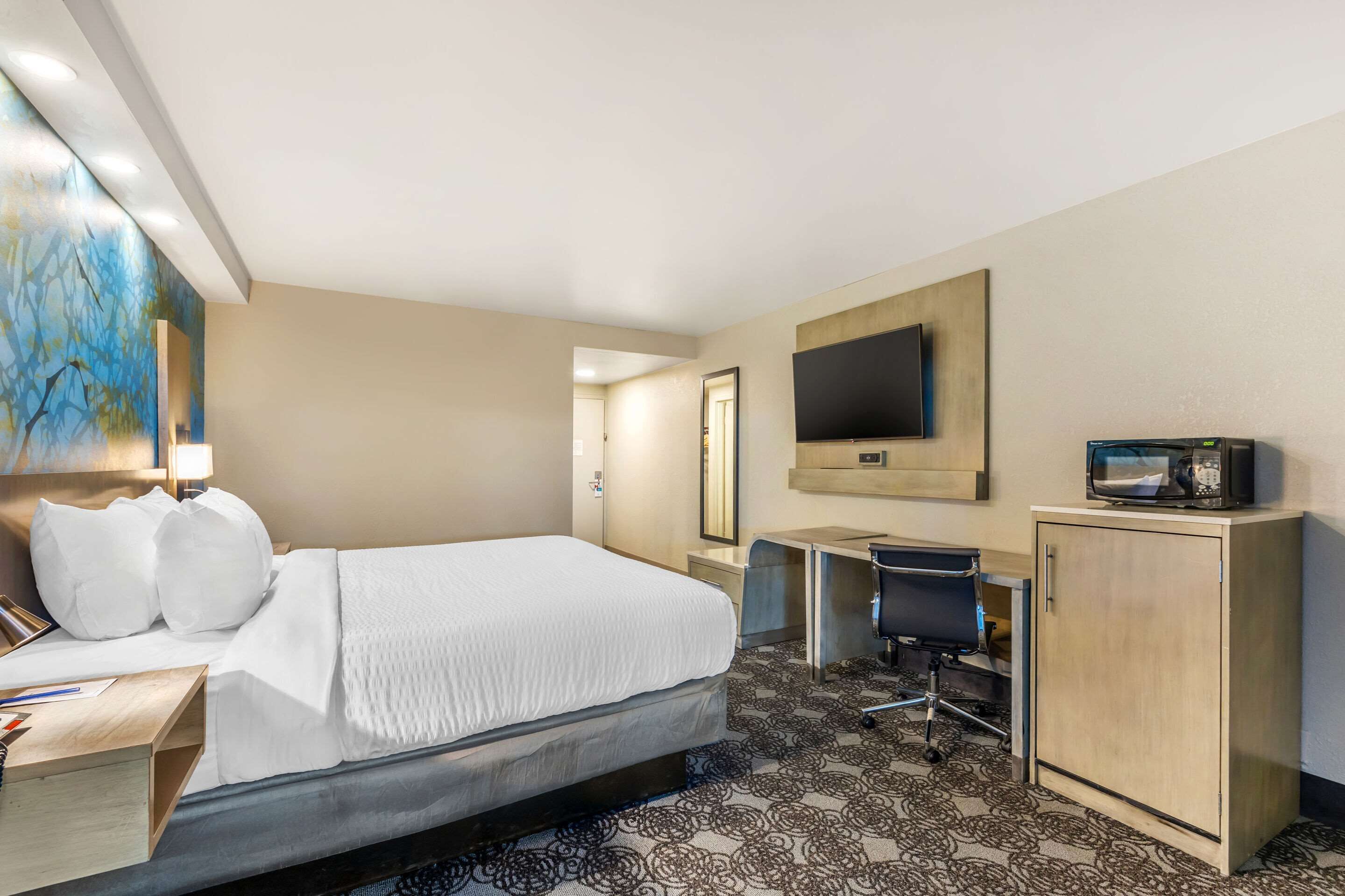 A hotel room with a bed, desk, chair, TV, and a cabinet.