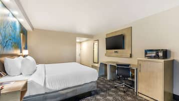 A hotel room with a bed, desk, chair, TV, and a cabinet.