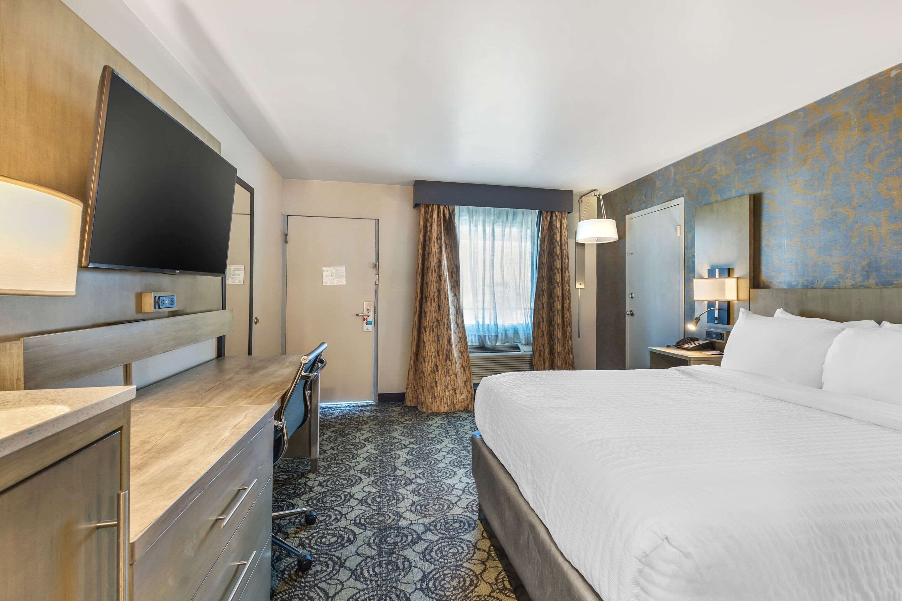 Una habitación de hotel con una cama, un escritorio, un televisor y una ventana con cortinas.