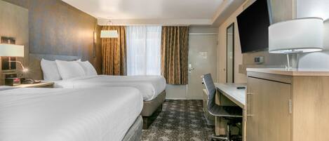 A hotel room with two beds, a desk, a chair, a TV, and a lamp.