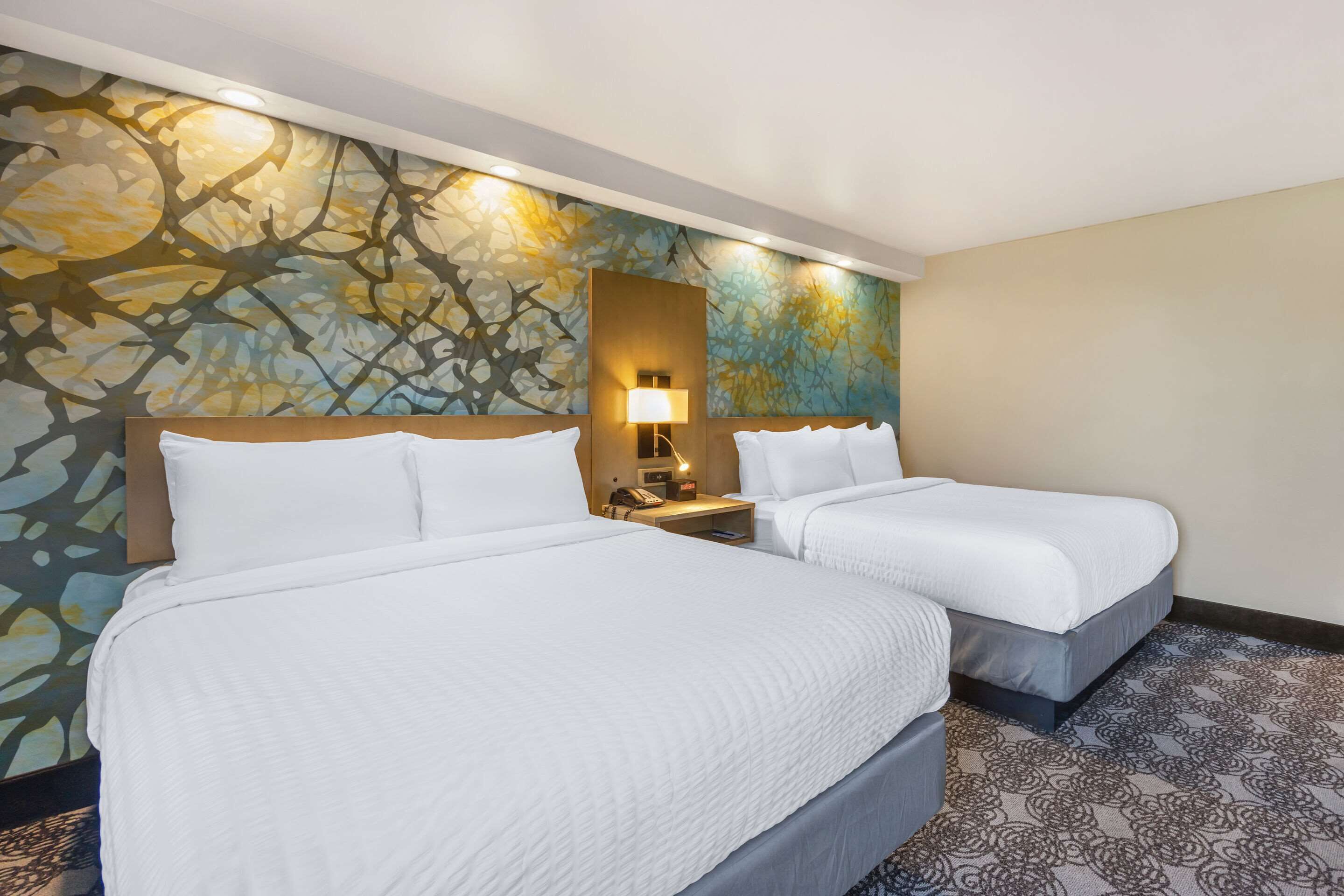 Une chambre d’hôtel avec deux lits, une moquette à motifs et une fresque murale.