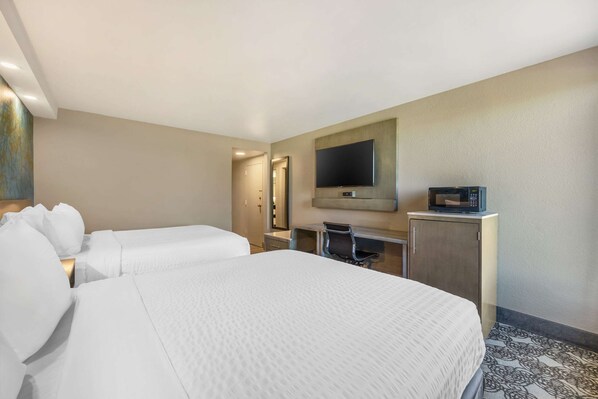 Una habitación de hotel con dos camas, un escritorio, un televisor y un microondas.