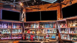 Un bar avec des étagères remplies de différentes bouteilles d’alcool, une caisse enregistreuse et une boîte de rhum Bacardi.