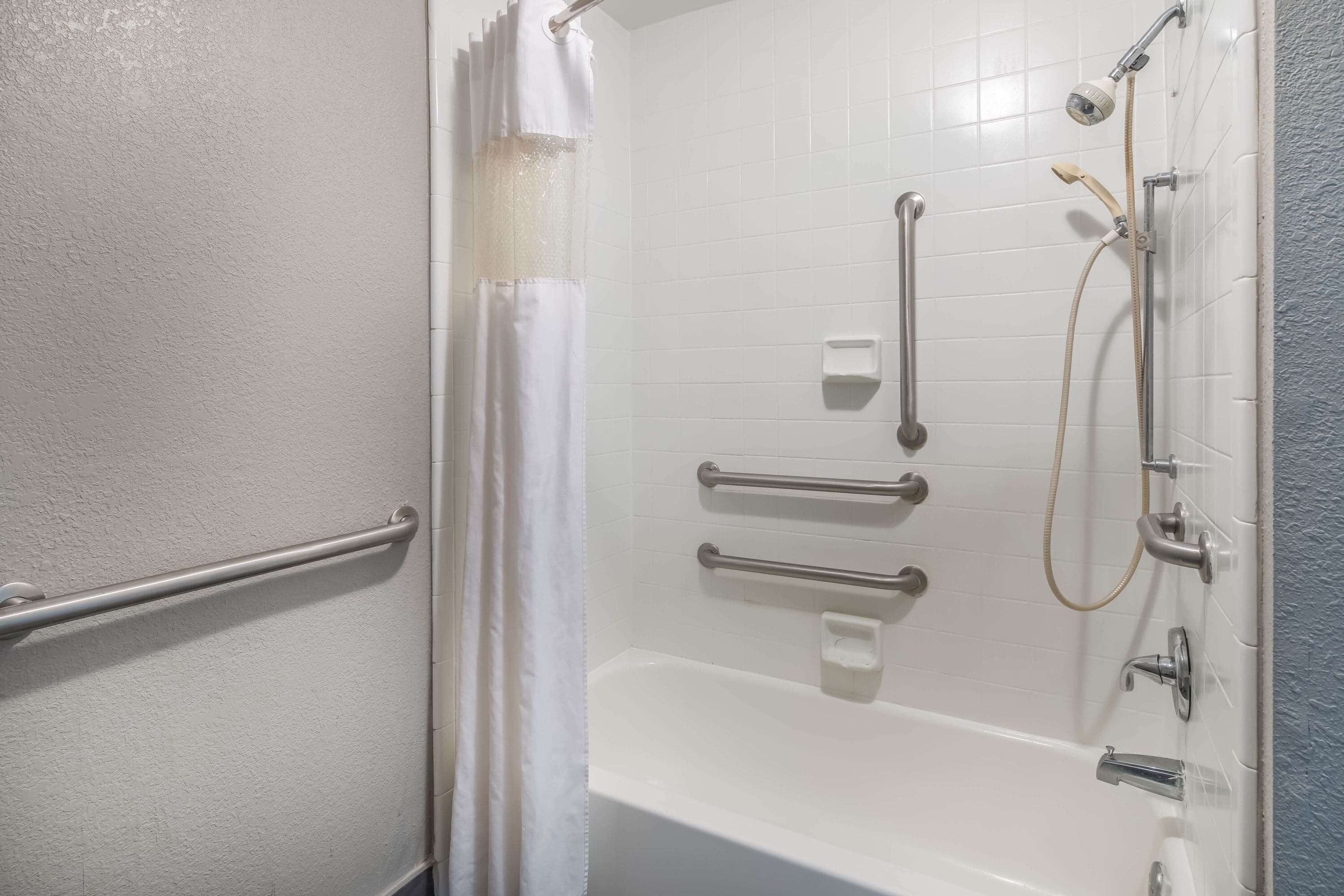 A bathroom with a bathtub, a shower, and grab bars.