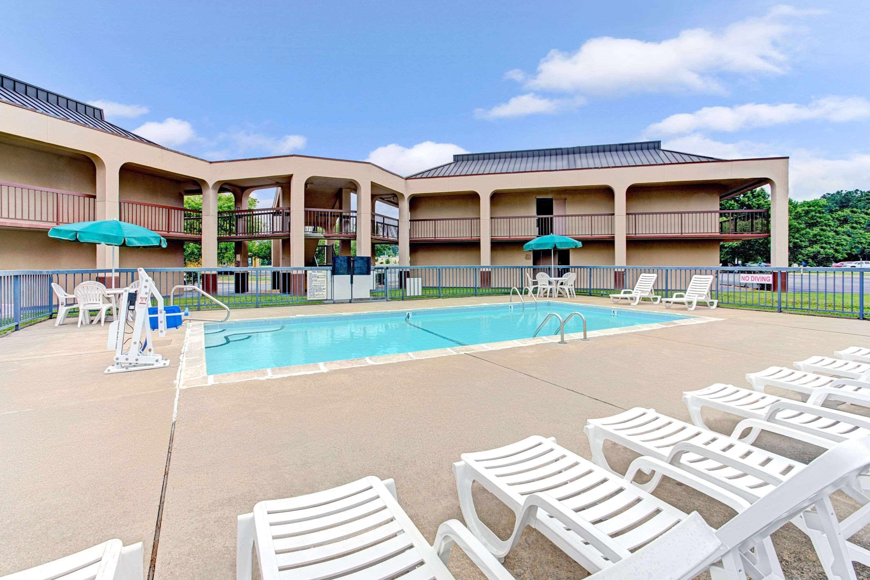 A pool area with white lounge chairs and umbrellas, a pool, and a building with multiple balconies.