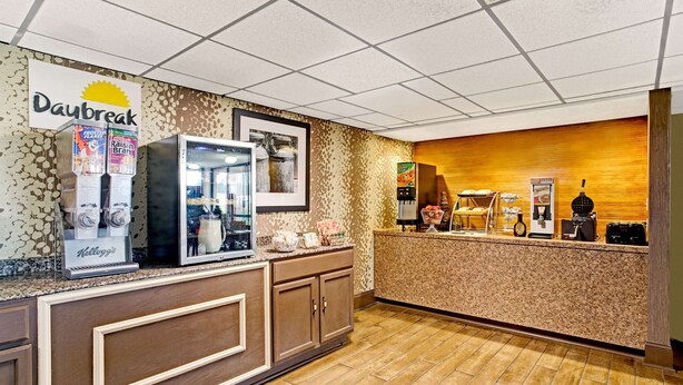 A breakfast area with a Daybreak sign, a refrigerator with beverages, a coffee machine, and a counter with a coffee dispenser. - Days Inn by Wyndham Wilson (Wilson)