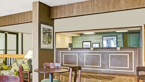 A reception area with a reception desk, framed pictures, and a seating area with chairs and a table. - Days Inn by Wyndham Wilson (Wilson)