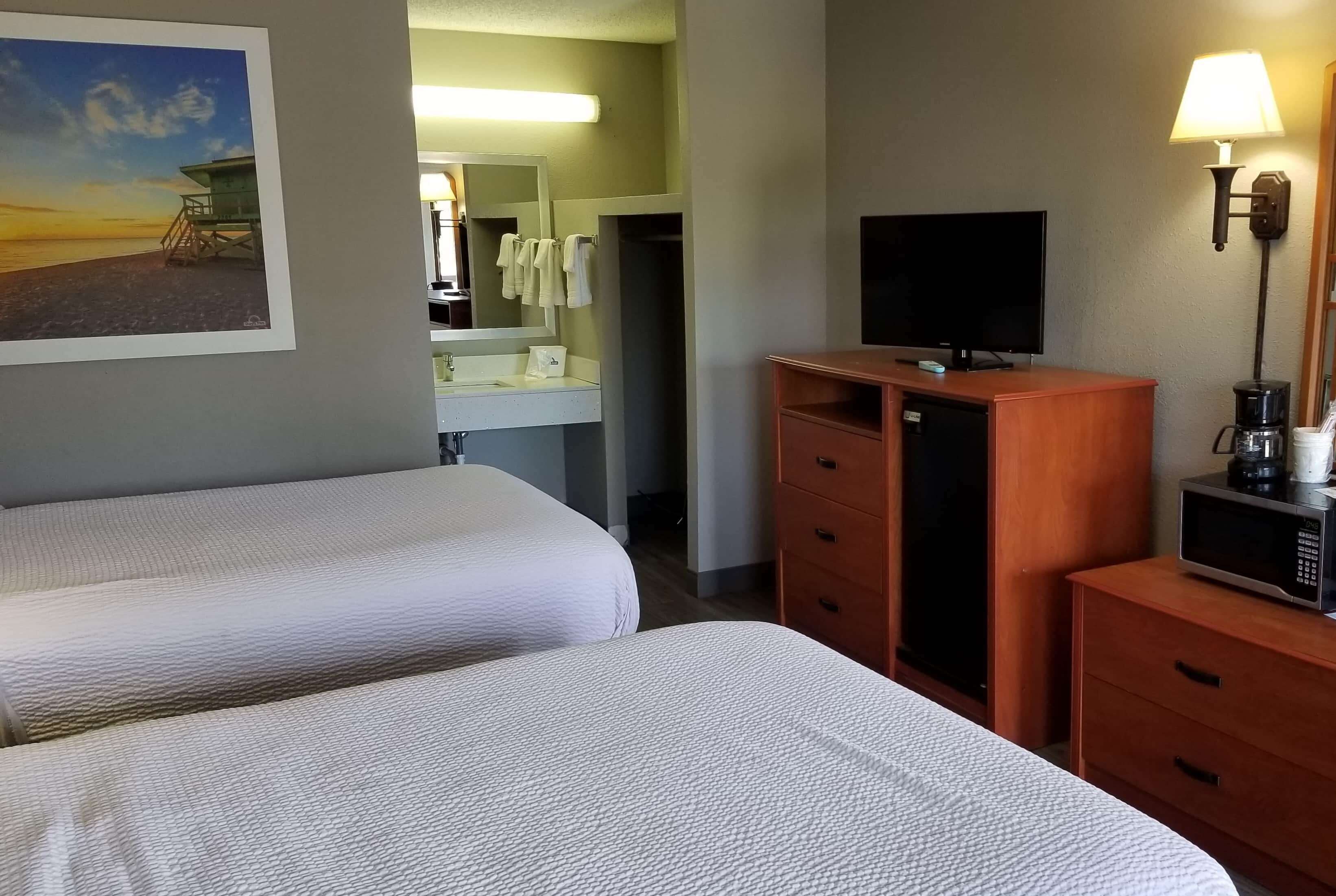 Une chambre d’hôtel avec deux lits, une télévision, une machine à café et un tableau représentant une scène de plage.