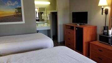 Une chambre d’hôtel avec deux lits, une télévision, une machine à café et un tableau représentant une scène de plage.