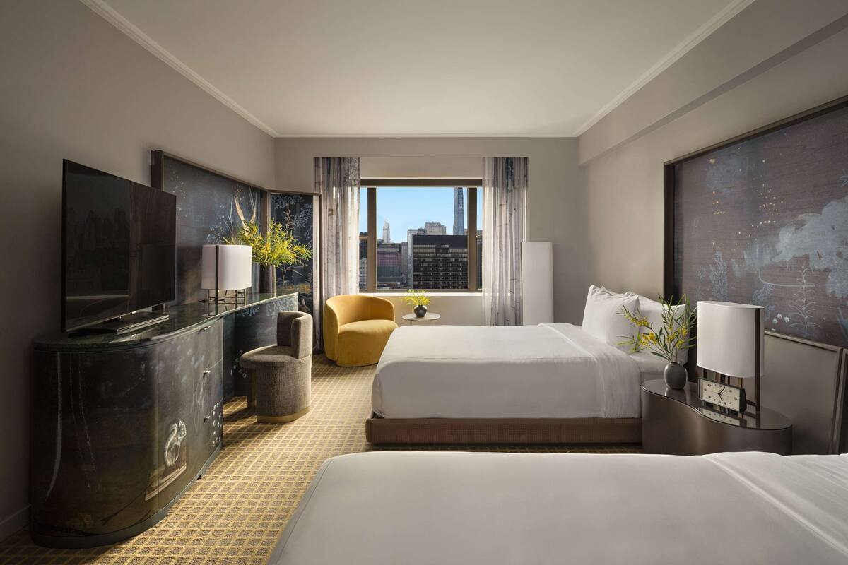 A hotel room with a large bed, a smaller bed, a TV, a desk, and a view of the city skyline.