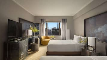 Une chambre d’hôtel avec un grand lit, un lit plus petit, une télévision, un bureau et une vue sur les toits de la ville.