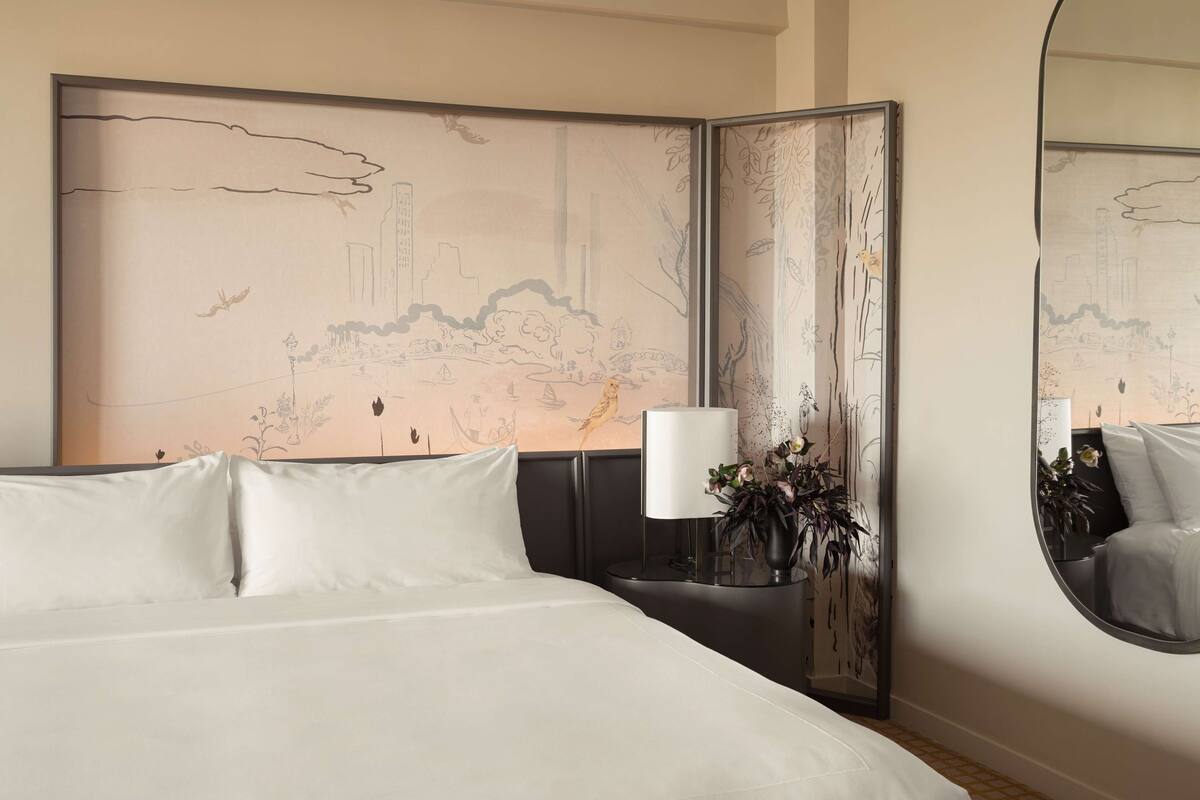 A hotel room with a large bed, a nightstand with a lamp, a mirror, and a decorative wall panel.