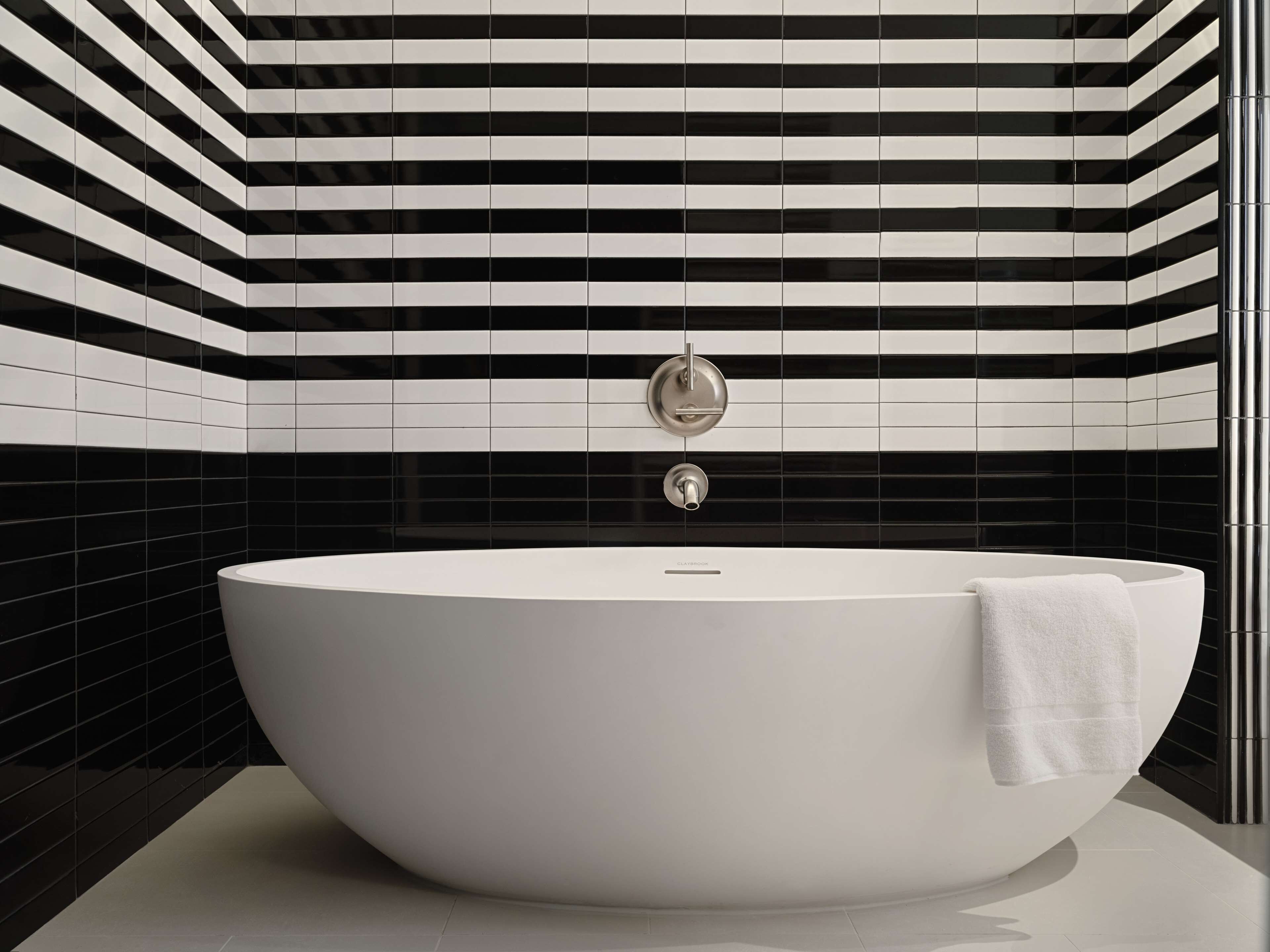 A modern bathroom with a large freestanding bathtub, black and white striped tiles on the walls, and a white towel on the edge of the tub.