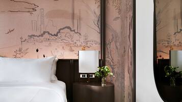 A hotel room with a bed, a nightstand with a lamp, a vase with flowers, and a wall with a mural.