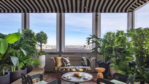 A sunlit room with a large window, a sofa, chairs, a coffee table, and various potted plants. - Park Lane New York (New York)