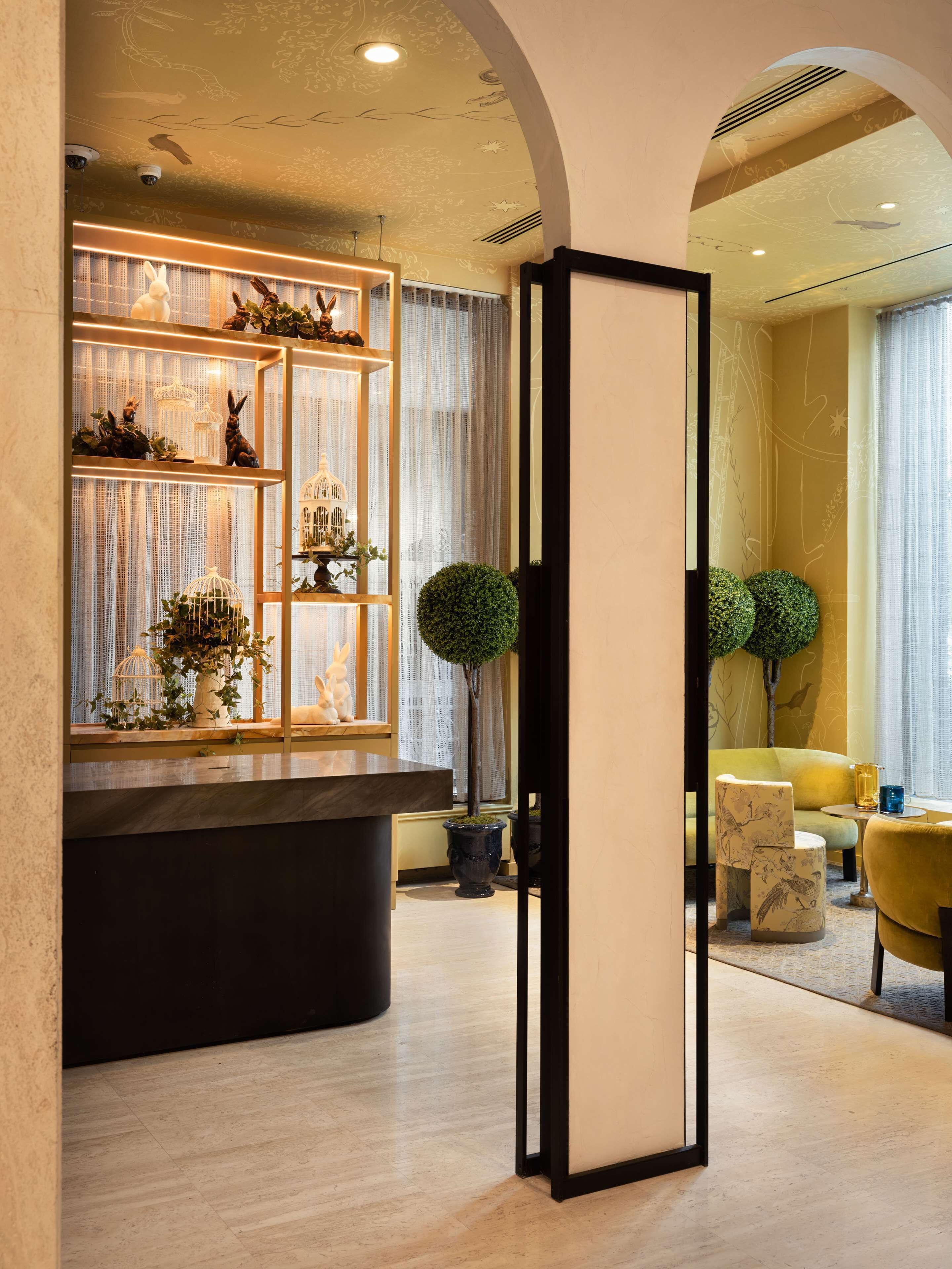 Un intérieur moderne comprenant un comptoir d’accueil, des étagères décoratives et un espace salon avec un fauteuil jaune et une table ronde.