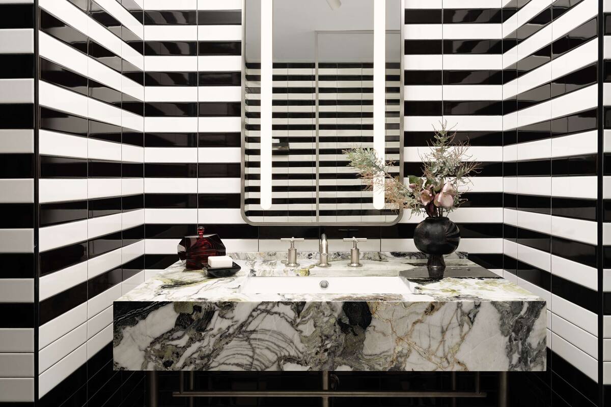 A modern bathroom with a black and white striped tile wall, a marble sink, and a vase with flowers.