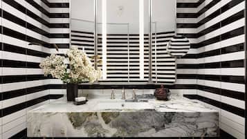 A bathroom with a black and white striped wall, a marble sink, and a mirror with three vertical lights.